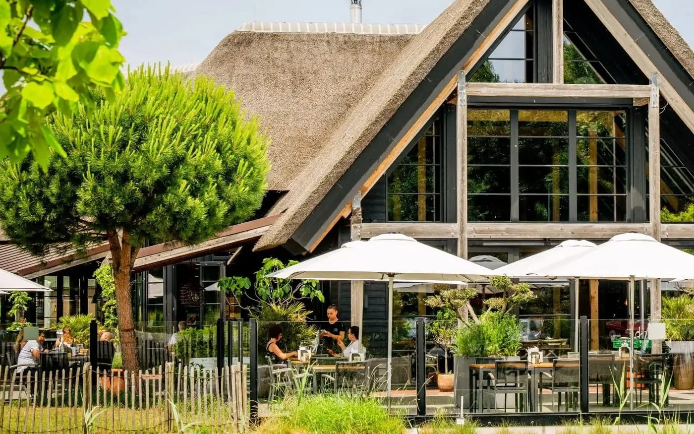 Het rieten pand van Venneper Lodge met parasols en gasten op het terras