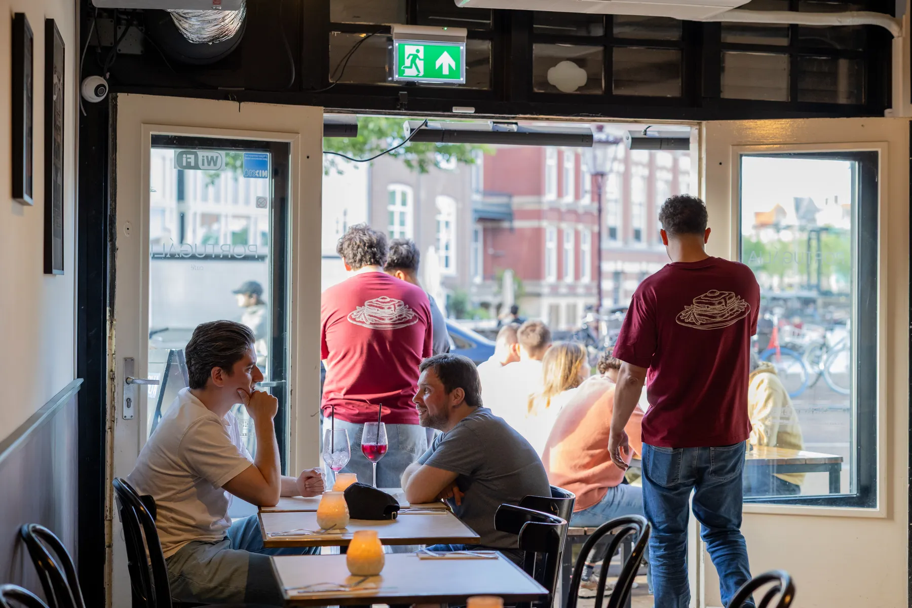 Gasten aan de raamtafels van Portugalia Churrasco in Rotterdam, met de bediening in de deuropening